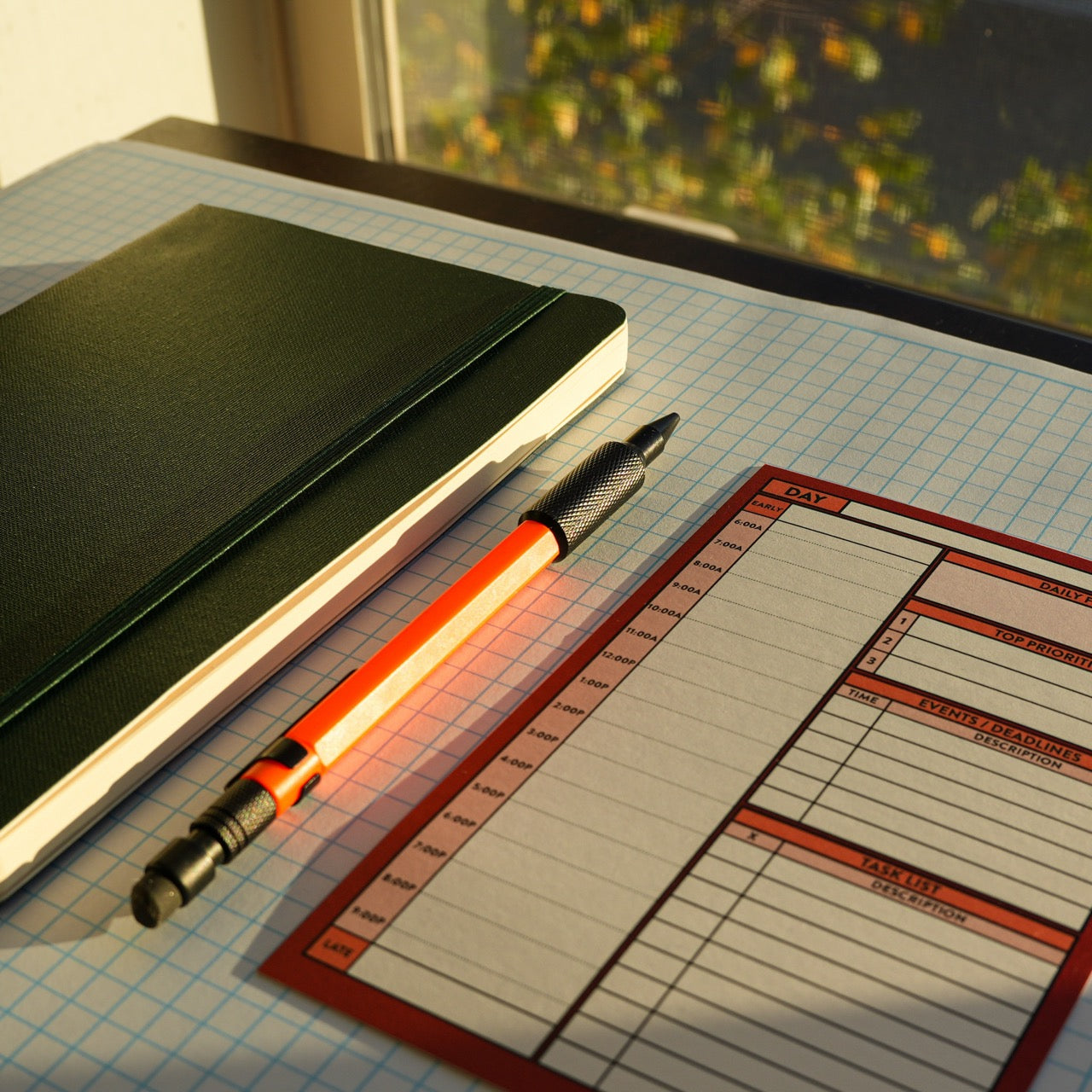 Better Made Plans Day planning card laying next a pencil and elastic-closure notebook on graph paper in front of a window.
