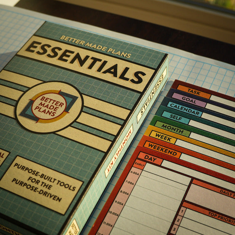 Packaging for the Better Made Plans Essentials kit with colorful planning cards stacked to the left. Background is graph grid paper.