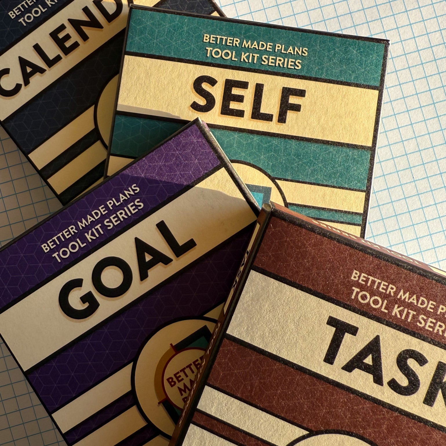 Packaging for Better Made Plans Calendar, Self, Goal, and Task planning cards laying stacked on a graph paper background.
