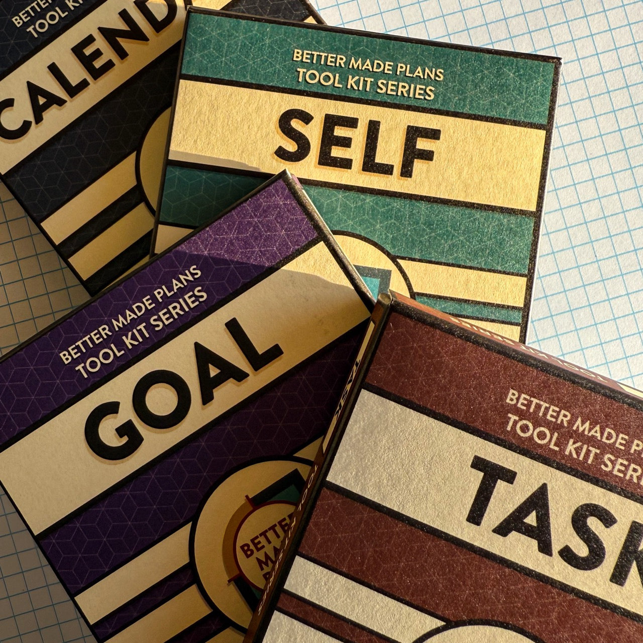 Product packaging for Better Made Plans Calendar, Self, Goal, and Task planning cards on a graph paper background.