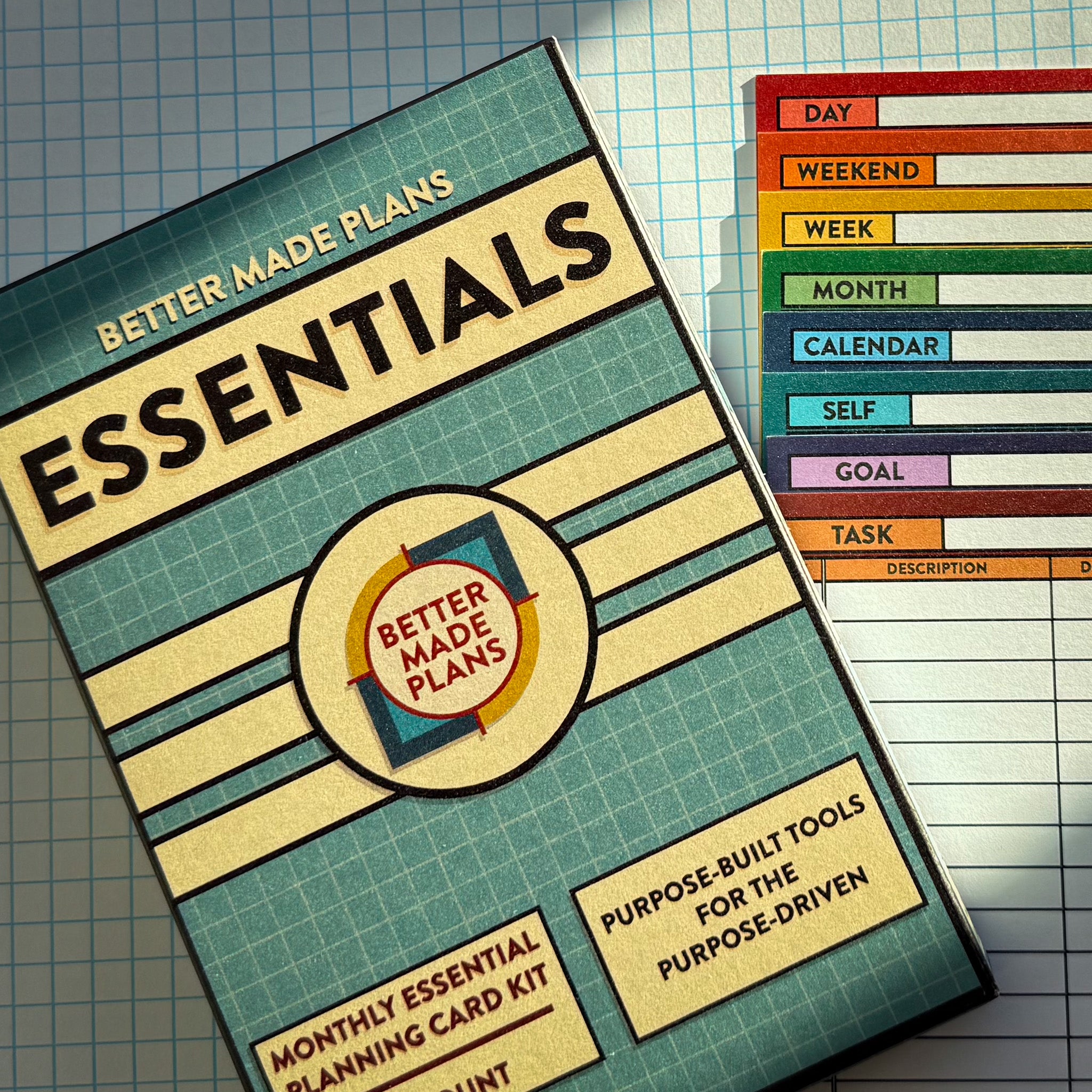 Packaging for Better Made Plans Essentials Planning Card kit next to a stack of all of the Better Made Plans planning cards on a graph paper background.