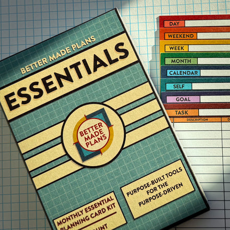 Packaging for Better Made Plans Essentials Planning Card kit next to a stack of all of the Better Made Plans planning cards on a graph paper background.